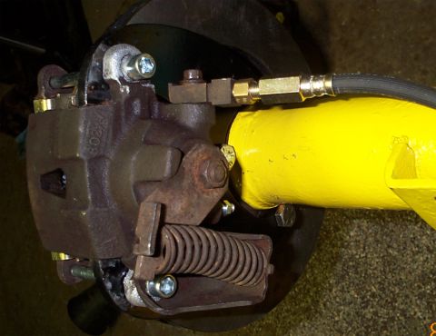 1986 Ford Bronco - Close-up of a completed rear disc brake conversion: a cast caliper with integral parking-brake lever and return spring mounted to a welded…