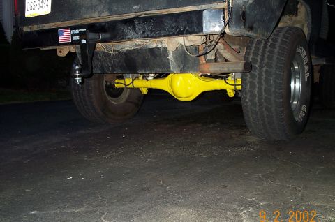 1986 Ford Bronco - Ground-level rear view under a black truck showing a freshly painted yellow solid rear axle housing with a bulbous center pumpkin, flanked…