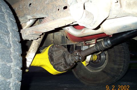 1986 Ford Bronco - Under-truck view of the installed yellow rear axle showing the bolt-on differential third member, driveshaft with U-joint, leaf spring, sho…