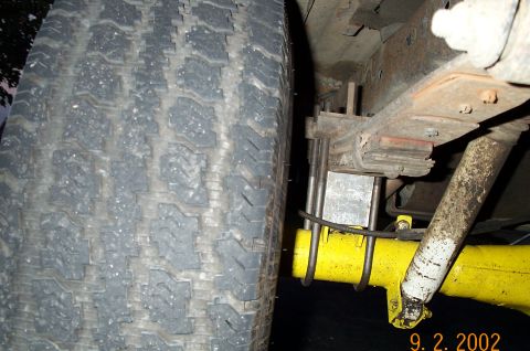 1986 Ford Bronco - Low-angle rear suspension shot showing a yellow-painted axle housing tube sitting under a leaf pack with a thick aluminum lift block and lo…