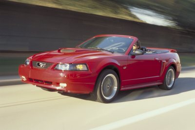 2003 Ford Mustang - A red 2003 Ford Mustang convertible is captured in motion on a road, its sporty design.