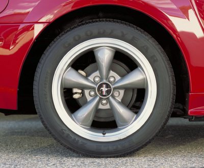 2003 Ford Mustang - A close-up view of a red vehicle's rear wheel and tire, a silver five-spoke rim with a Mustang emblem.