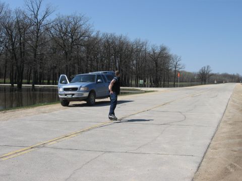 1976 Ford Ranchero - A man stands next to a blue pickup truck on a road with water on the side.