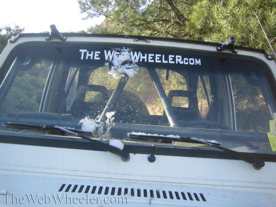 White Suzuki Samurai windshield with "THE WHEELER.COM" sticker and some snow
