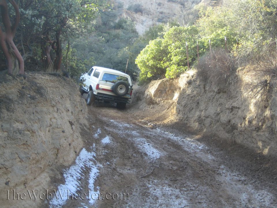 White SUV with spare tire on rear driving on muddy trail