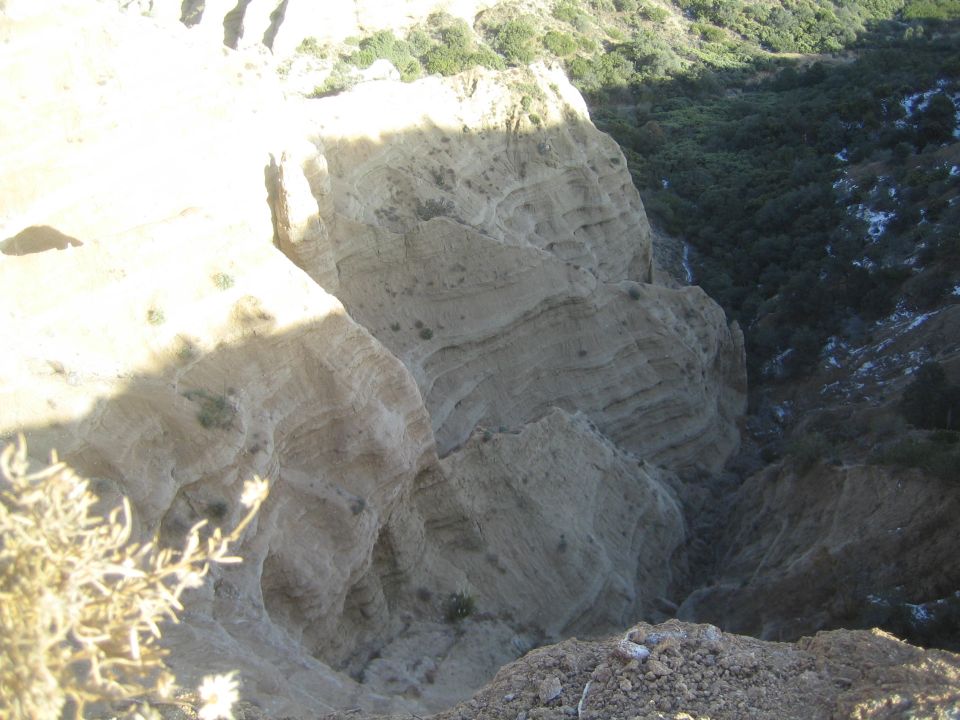 view from above into a deep canyon with layered rock formations and sparse vegetation