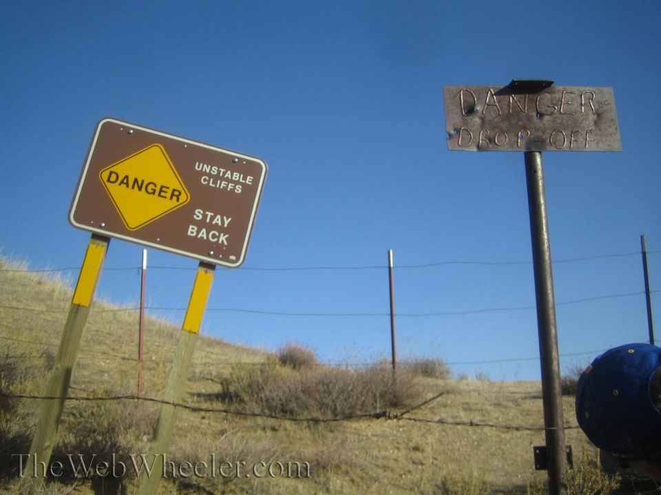 Danger signs warning of unstable cliffs and a drop off against a clear blue sky