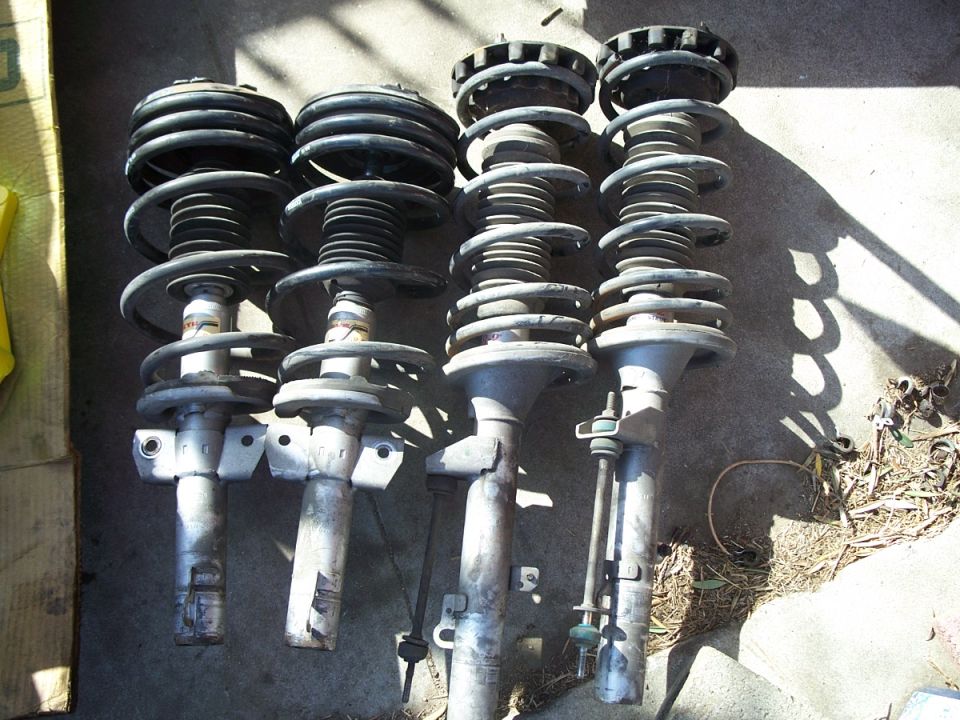 Four used car struts with coil springs, laid out on concrete