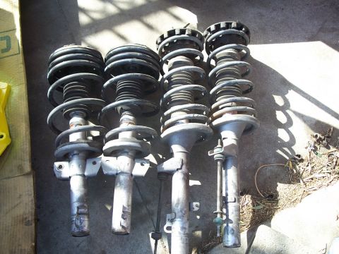 1993 Ford Taurus - Four suspension struts with coil springs are laid out on the ground.
