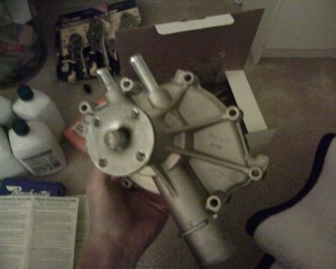 1995 Ford Bronco - A water pump part is held in a hand, with other automotive items scattered around the floor.