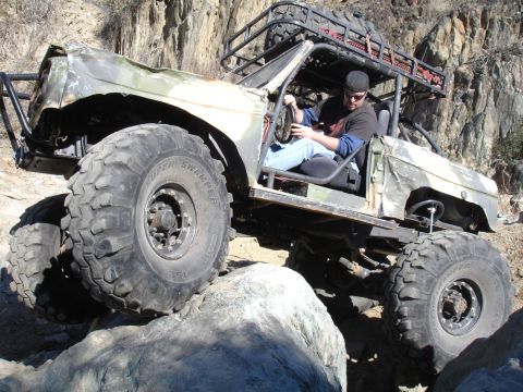 1966 Ford Bronco - A heavily modified off-road vehicle navigates a rocky terrain with a driver at the wheel.