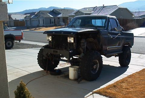 1986 Ford Bronco - This heavily modified Ford Bronco features a lifted suspension and oversized tires, parked outside a suburban home.