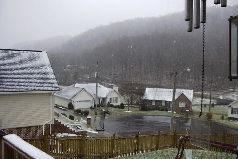 1995 Ford Bronco - A winter scene with snow falling on houses and a wooded hillside, obscuring any vehicles.