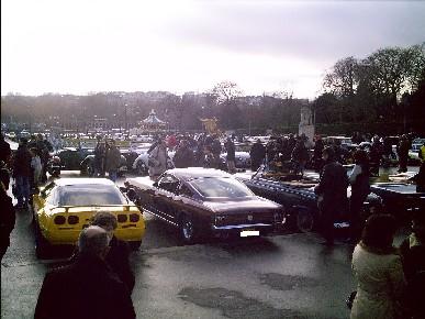 1991 Ford Crown Victoria - An outdoor gathering of cars and people under a cloudy sky, with a carousel visible in the background.