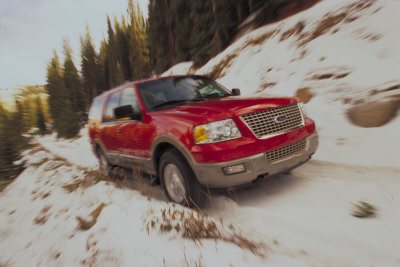 2003 Ford Expedition - A red SUV navigates a snowy, mountainous terrain, kicking up snow as it drives.