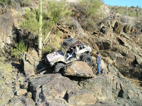 1966 Ford Bronco - An off-road vehicle navigates a difficult rocky terrain, with a person observing its progress.
