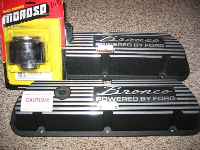 Pair of black Ford Bronco valve covers with silver stripes and 'Bronco POWERED BY FORD' text, next to a yellow Moroso oil filter package
