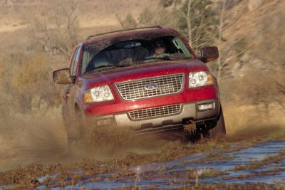2003 Ford Expedition - A red 2003 Ford Expedition navigates a muddy terrain, kicking up dirt and water.
