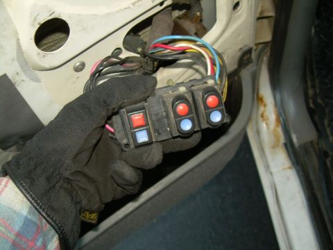 1988 Ford Bronco - Gloved hand holds a door lock switch assembly with red and blue buttons, disconnected from wiring.