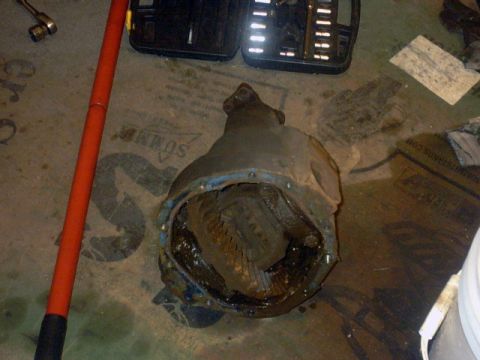 1989 Ford Bronco - Differential assembly removed from a vehicle, resting on the floor next to tools and shop supplies.