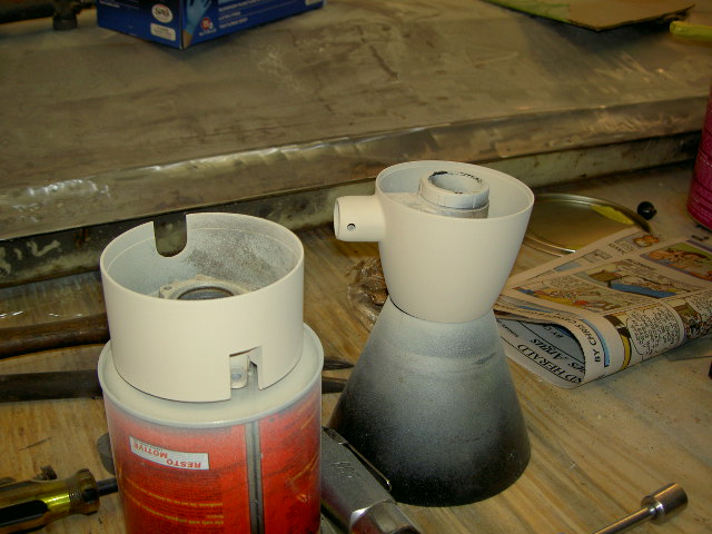 Two white plastic automotive parts, one on a red can, next to a newspaper