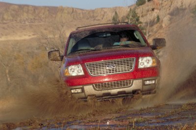 2003 Ford Expedition - A red 2003 Ford Expedition navigates a muddy terrain, kicking up water and dirt.
