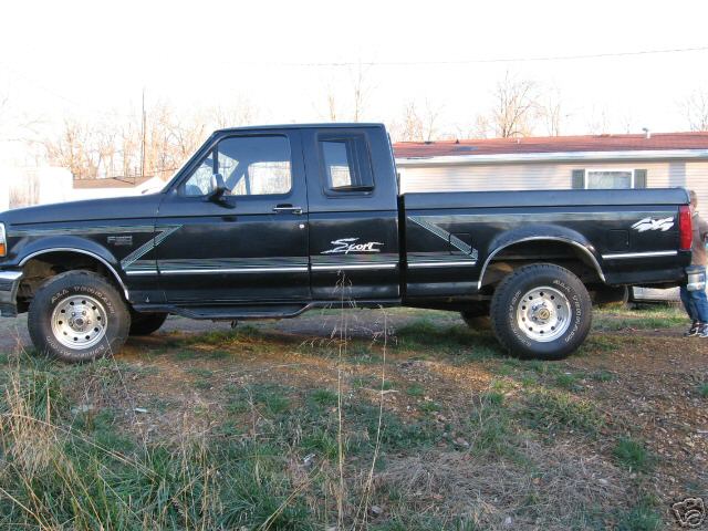 Black Ford extended-cab 4x4 pickup with Sport graphics, side view, parked on grass