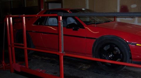 1988 Pontiac Fiero - A red 1988 Pontiac Fiero is visible from the side, partially obscured by a red safety railing.
