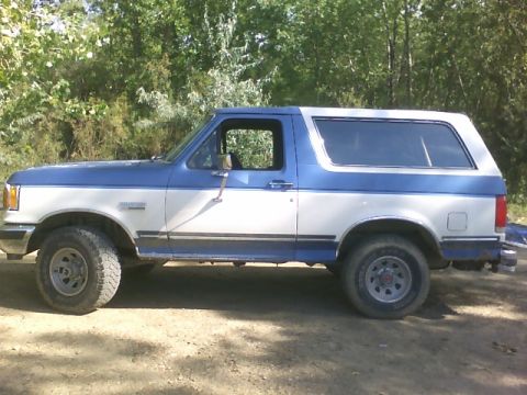1989 Ford Bronco - This two-tone Ford Bronco is parked outdoors with trees visible behind it.