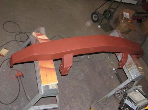 2000 Chevrolet Tahoe - A vehicle bumper, coated in red primer, is supported by sawhorses in a workshop setting.