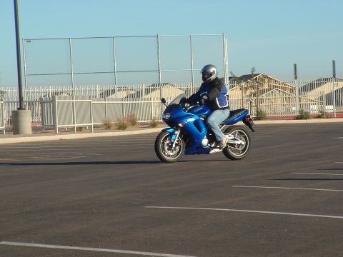 2007 Kawasaki Ninja - A rider on a blue Kawasaki Ninja motorcycle cruises through an empty parking lot under a clear blue sky.