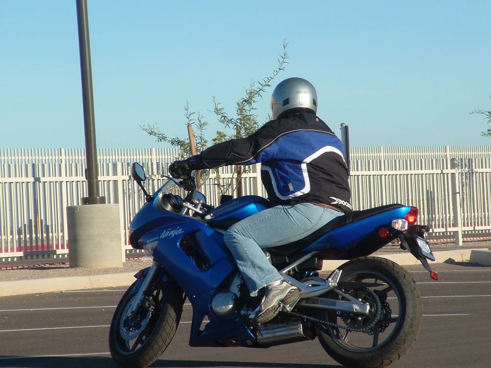 Blue Kawasaki Ninja motorcycle with a rider wearing a silver helmet and blue/black jacket, seen from the side