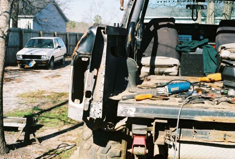 1978 Ford Bronco - Tools and parts are laid out in the bed of a vehicle, with another car visible in the yard.