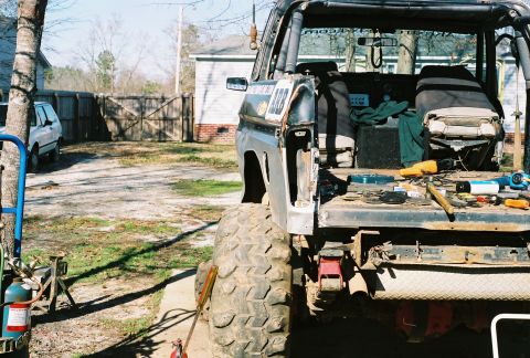 1978 Ford Bronco - A heavily modified off-road vehicle's interior and rear are visible, with tools scattered on the bed and a white SUV parked nearby.