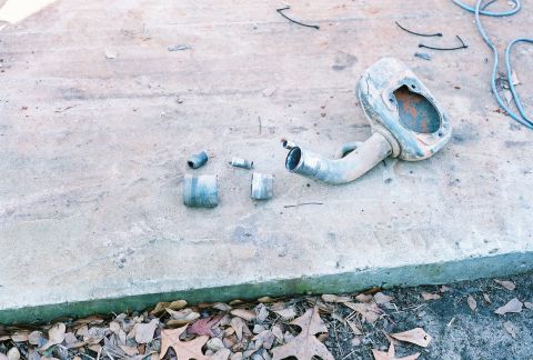 1978 Ford Bronco - Various exhaust pipe and muffler components are scattered on a concrete surface next to fallen leaves.