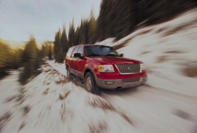 2003 Ford Expedition - A red 2003 Ford Expedition navigates a snow-covered path, with trees lining the side of the road.