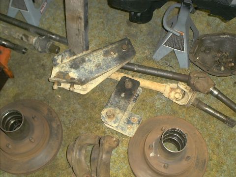 1986 Ford Bronco - Various automotive parts, including drive shafts and brake rotors, are scattered on a carpeted surface.
