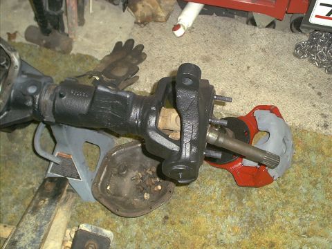 1986 Ford Bronco - Front axle assembly components, including a U-joint and brake caliper bracket, are laid out on the floor.