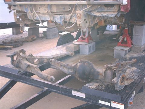 1986 Ford Bronco - Vehicle front axle and suspension parts are disassembled and placed on a trailer for transport or repair.