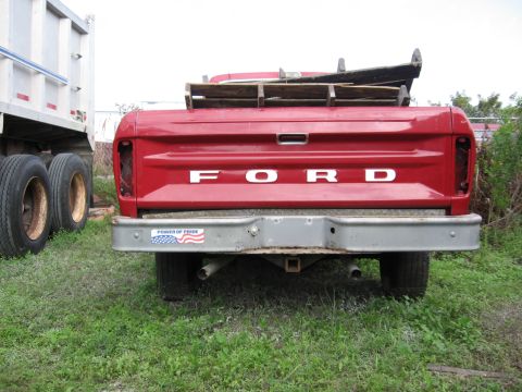 1974 Ford F-100 - The rear of a red Ford pickup truck is shown, parked next to a large white dump truck.