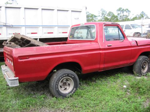 1974 Ford F-100 - A red Ford pickup truck is parked outdoors, with a large white trailer behind it.