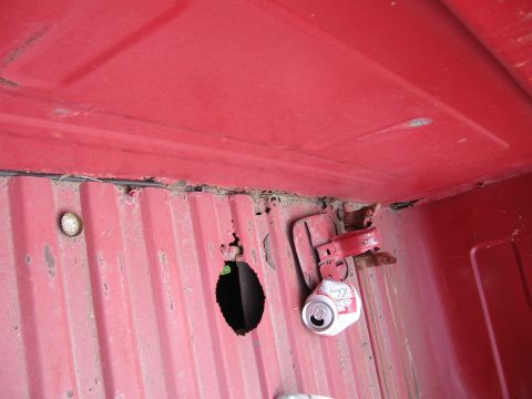 1974 Ford F-100 - A close-up view of a damaged red truck bed shows signs of wear and tear, including rust and a discarded beverage can.