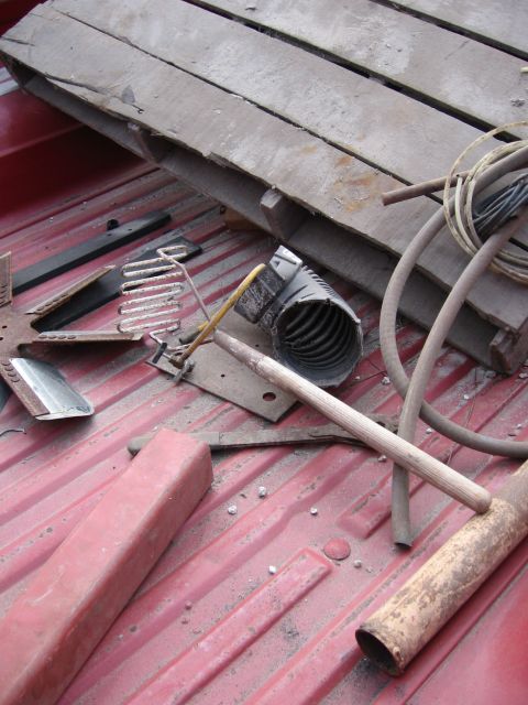 1974 Ford F-100 - The bed of a red pickup truck is filled with assorted items, including a wooden pallet and various metal and plastic components.