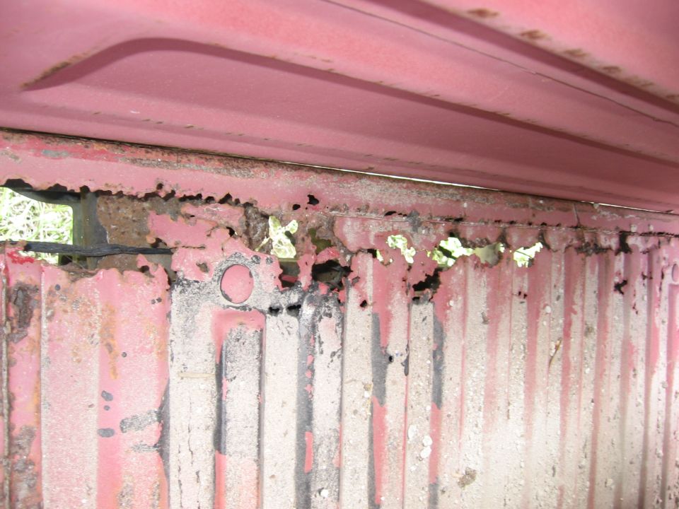 Close-up of heavily rusted red metal panel with vertical ridges and holes