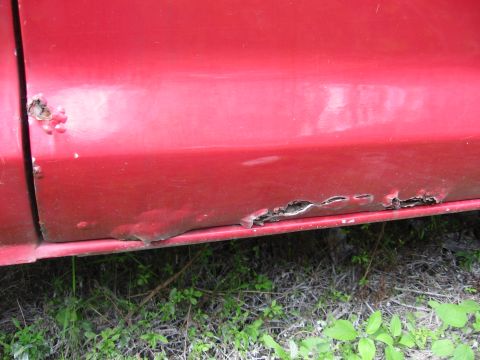 1974 Ford F-100 - The lower body panel of a red truck shows significant rust damage and corrosion.