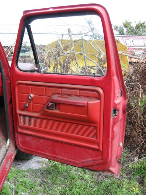 1974 Ford F-100 - Interior of a red truck door, showing the paneling and window mechanism.
