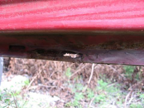 1974 Ford F-100 - The lower body panel of a vehicle shows significant rust and a hole, indicating damage.