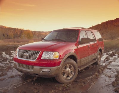 2003 Ford Expedition - A red 2003 Ford Expedition navigates a muddy terrain under a warm sunset sky.