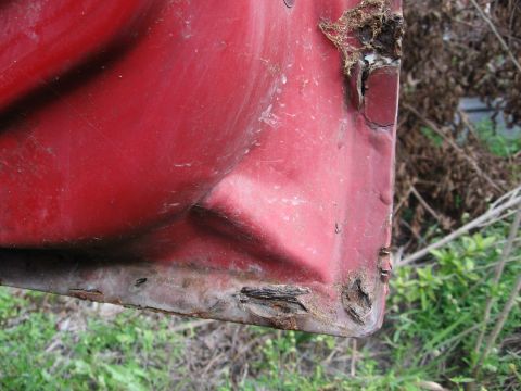 1974 Ford F-100 - Close-up view of a red truck door's lower corner, revealing extensive rust and corrosion.