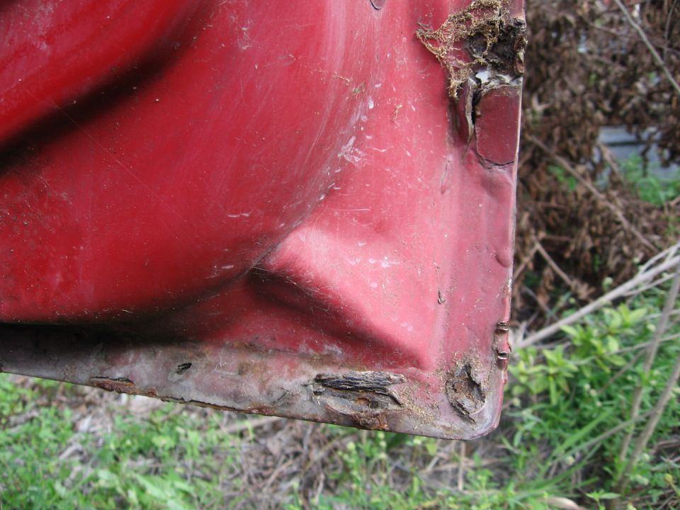 Red truck door corner showing significant rust damage along the bottom edge